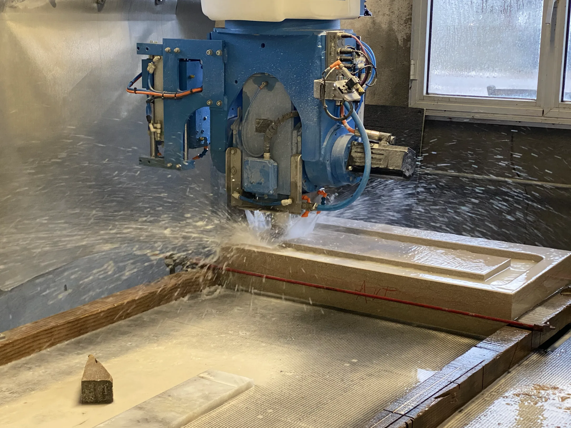 Découpe d'une pierre sous jet d'eau sur une machine à commande numérique, dans un atelier de marbrerie